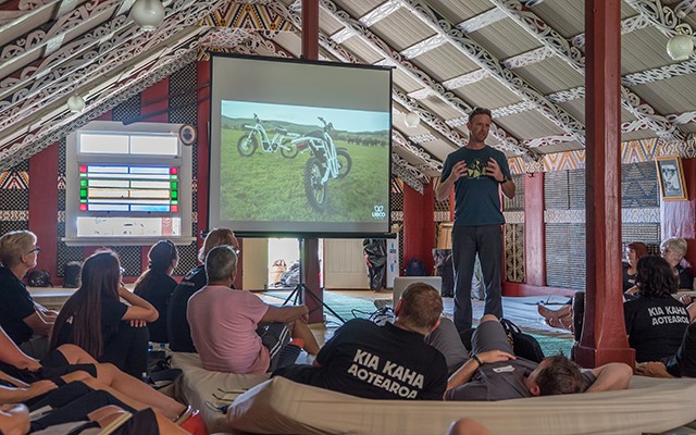 Man photographed giving presentation to colleagues in a wharenui on a marae