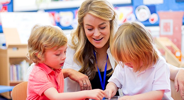 Teacher aide helping two small children in a classroom